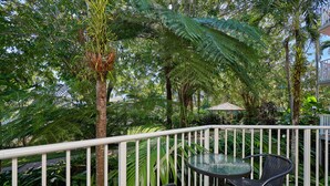 An outdoor patio with a table and chairs, surrounded by lush greenery and a white railing. - Tropical Oasis near Beach (Holloways Beach)