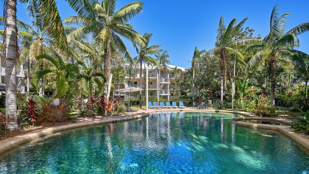A clear pool surrounded by palm trees and a multi-story building with balconies. - Tropical Oasis near Beach (Holloways Beach)