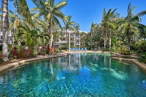 Una piscina cristalina rodeada de palmeras y un edificio de varios pisos con balcones.
