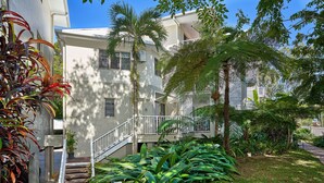 A multi-story building with a central staircase, surrounded by lush greenery and palm trees. - Tropical Oasis near Beach (Holloways Beach)