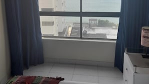 Quarto com uma janela grande, uma cama, cômoda e tapete estampado.