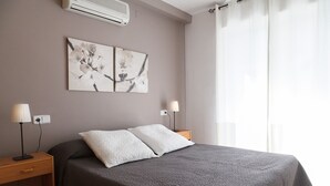 A bedroom with a bed, two bedside tables, a wall-mounted air conditioner, and a window with curtains. - UHC LARIMAR - Fantastic family apartment with swimmingpool (Salou)