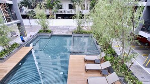 Una piscina en la azotea con piso de baldosas, terraza de madera y sillas de descanso.