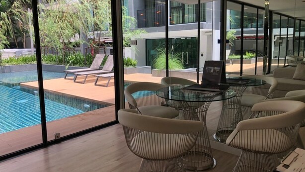Un espacio interior moderno con una pared de vidrio que da a una piscina y follaje.