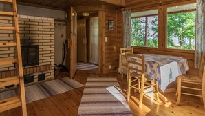 En stuga byggd av trä med ett sovloft, en matplats med bord och stolar samt en öppen spis.