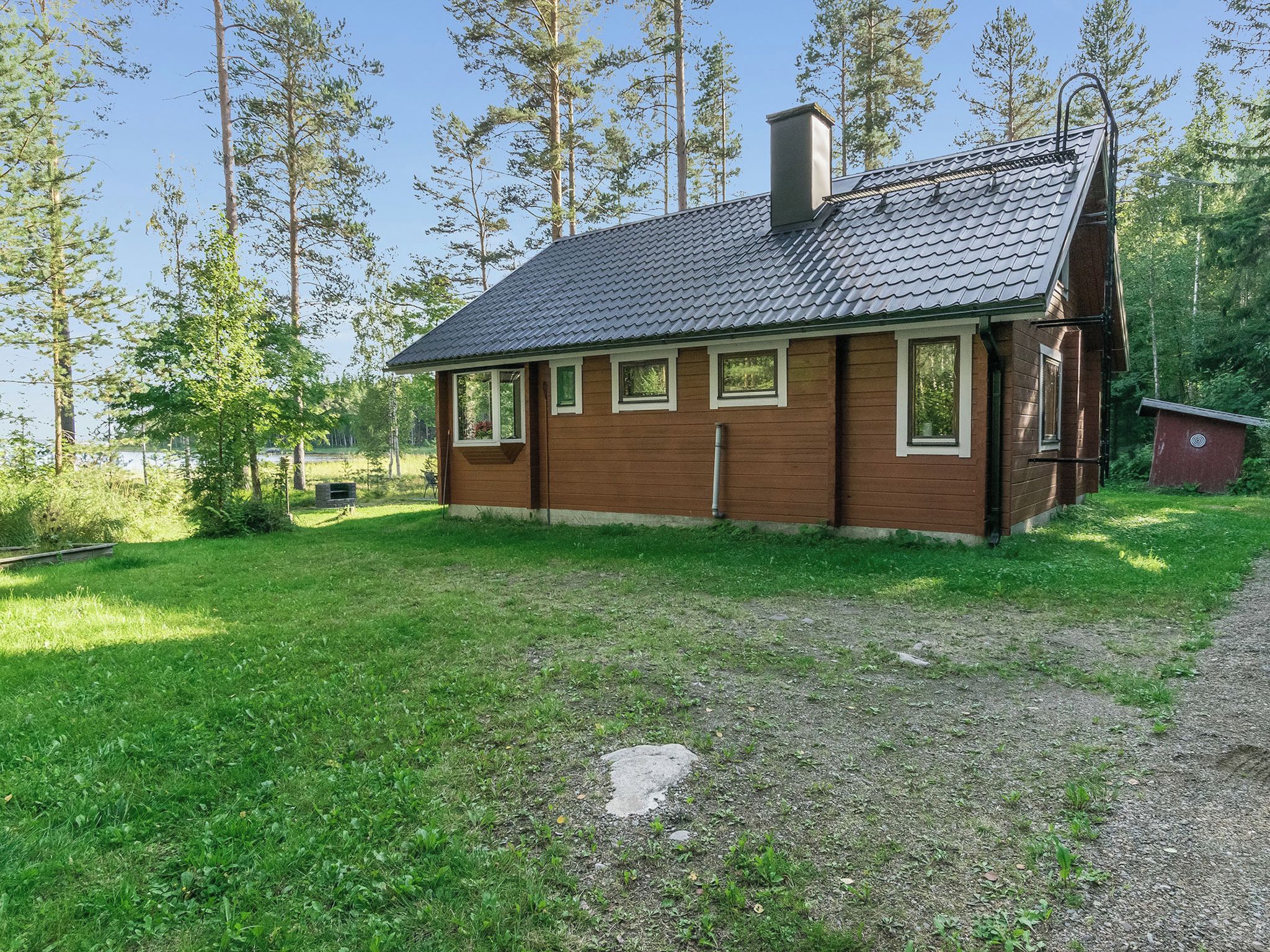 A small wooden house with a sloped roof, surrounded by a grassy yard and tall trees.