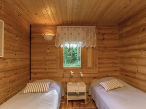 A cabin room with two beds, a window with a view of trees, a bedside lamp, and a small table.