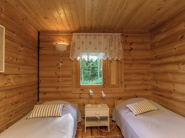 Une cabine comprenant deux lits, une fenêtre donnant sur la forêt, une lampe de chevet et une petite table.