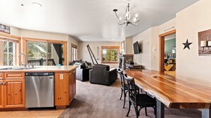 A spacious kitchen with wooden cabinets, a dishwasher, and a large island. There is a dining area with a wooden table and chairs. - Private Balcony w/ Mountain Views in River Run, Short Walk to Everything! (Keystone)