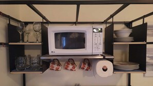 Une cuisine avec un four à micro-ondes posé sur une étagère, entouré de verres à vin, d’assiettes et d’un rouleau d’essuie-tout.