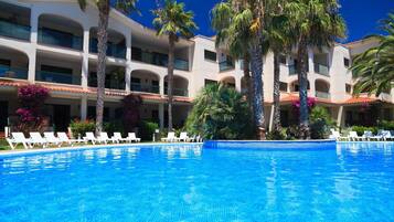 Un hotel con piscina, palmeras y sillas de descanso blancas.