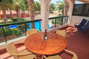 Une table ronde en bois, entourée de six chaises, une bouteille de vin et des verres à vin, le tout sur un balcon offrant une vue sur une piscine et des palmiers.