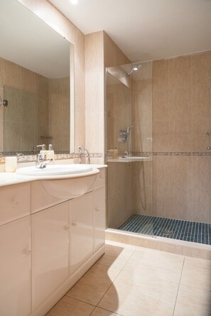 Une salle de bain moderne dotée d’une douche à parois de verre, d’un grand miroir et d’un meuble-lavabo avec un évier et des placards de rangement.