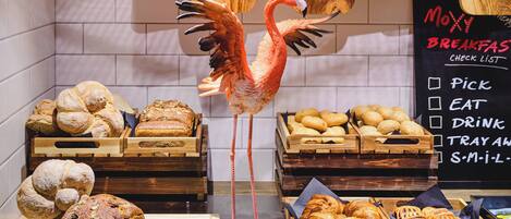 Un bufé de desayuno con panes y pastelería variados, una decoración de flamenco y un menú en pizarra que enumera las opciones de desayuno.