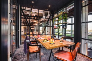A modern conference room with a long table, chairs, and a view of the outdoors through large windows. - Moxy Poznan Airport (Poznan)