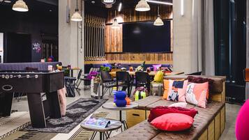 Un área de lounge moderna con mesa de fútbol, asientos cómodos y una zona de bar.