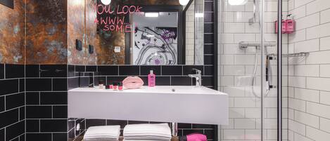 A modern bathroom with a white sink, black and white tiles, a mirror, and a pink hairdryer on a shelf.