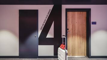 A hotel room with a large number '14' on the wall, a wooden door, and a suitcase with a red bag.