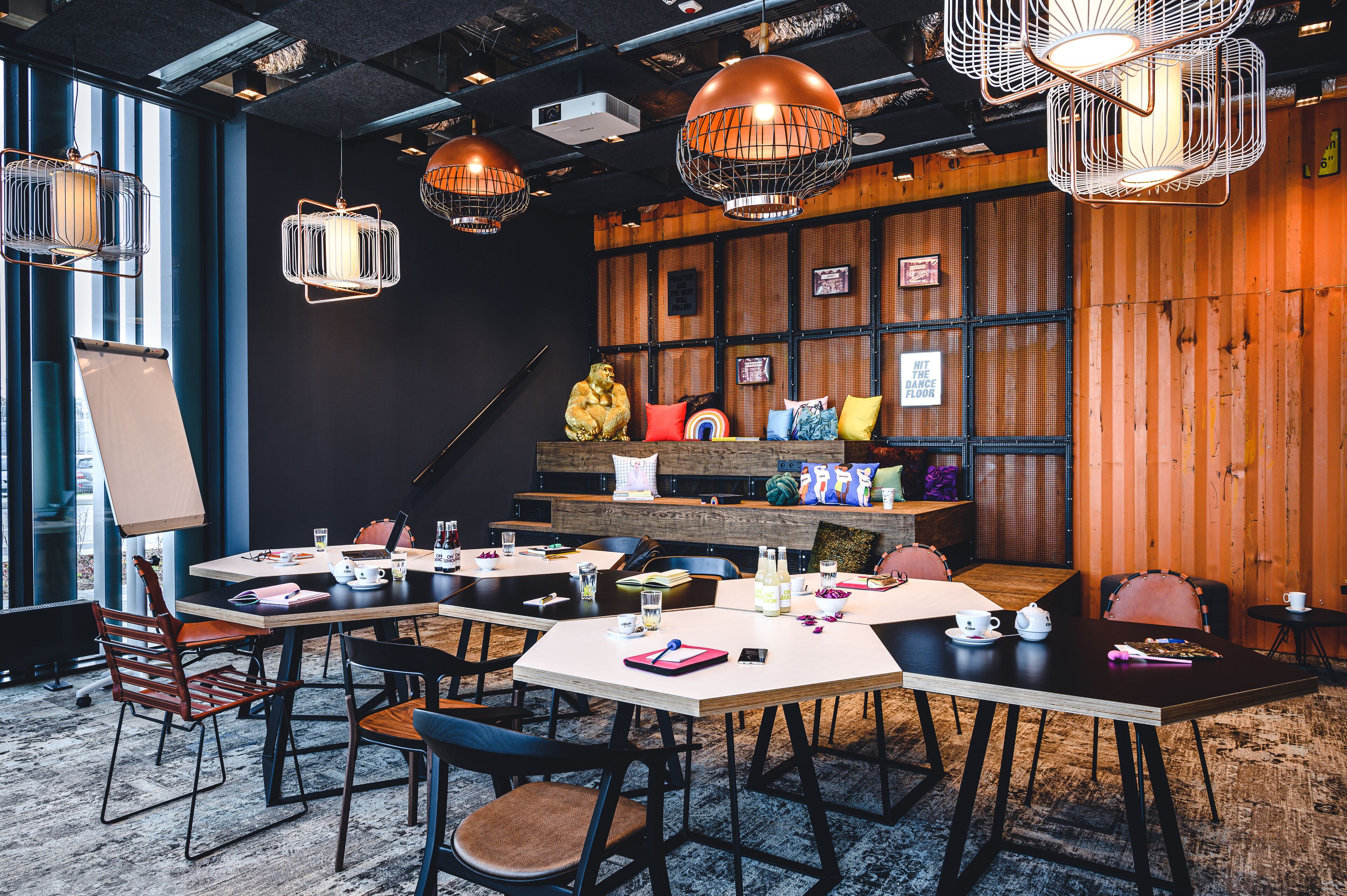 Een moderne vergaderruimte met tafels, stoelen en hangende pendelverlichting.