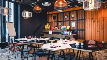 Een moderne vergaderruimte met tafels, stoelen en hangende pendelverlichting.