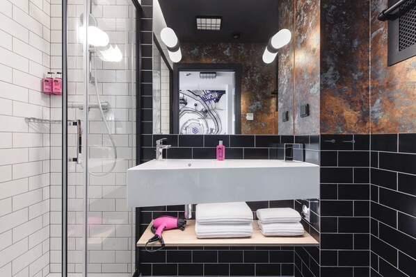 A modern bathroom with a glass shower enclosure, a white sink with a mirror above, and black and white tiled walls. - Moxy Poznan Airport (Poznan)