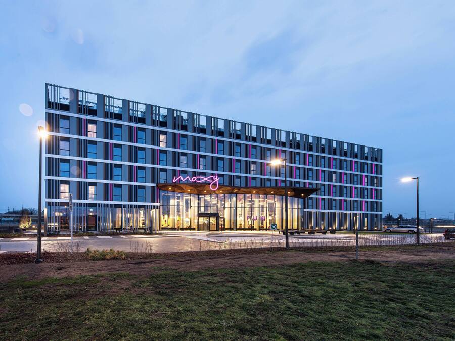 Un hôtel moderne avec une façade en verre, un panneau lumineux au néon et une entrée bien éclairée.