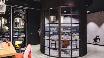 Ein modernes Interieur mit einem runden Tisch und Stühlen, einer Glastrennwand mit Kreideanschriften und Blick auf die Stadt durch große Fenster.