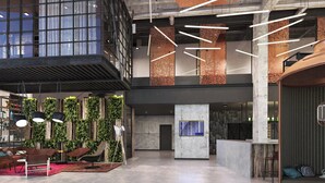 Een ruime lobby met een hoge plafond, moderne verlichtingsarmaturen en een zithoek met een rood tapijt.