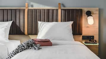 Ein Hotelzimmer mit Holz-Kopfteil, weißer Bettwäsche, einer tischigen Decke, einer roten Handtasche und einem Nachttisch mit Lampe und Gläsern.