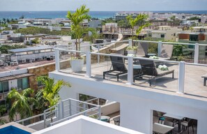 A rooftop terrace with lounge chairs, potted plants, and a view of the city and ocean.