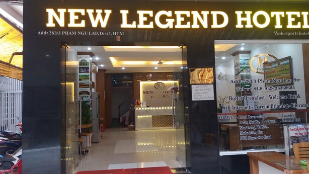 New Legend -hotellin sisäänkäynti, jossa on vastaanottotiski, kello ja kyltti, jossa luetellaan hotellin tarjoamat palvelut, kuten aamiainen buffet-tyyliin, Wi-Fi ja ilmastointi.