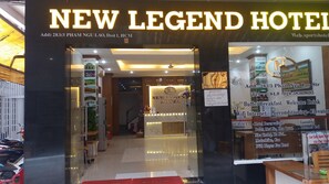 The entrance of New Legend Hotel with a reception desk, a clock, and a signboard listing amenities like buffet breakfast, wifi, and air conditioning. - New Legend Hotel (Ho Chi Minh City)