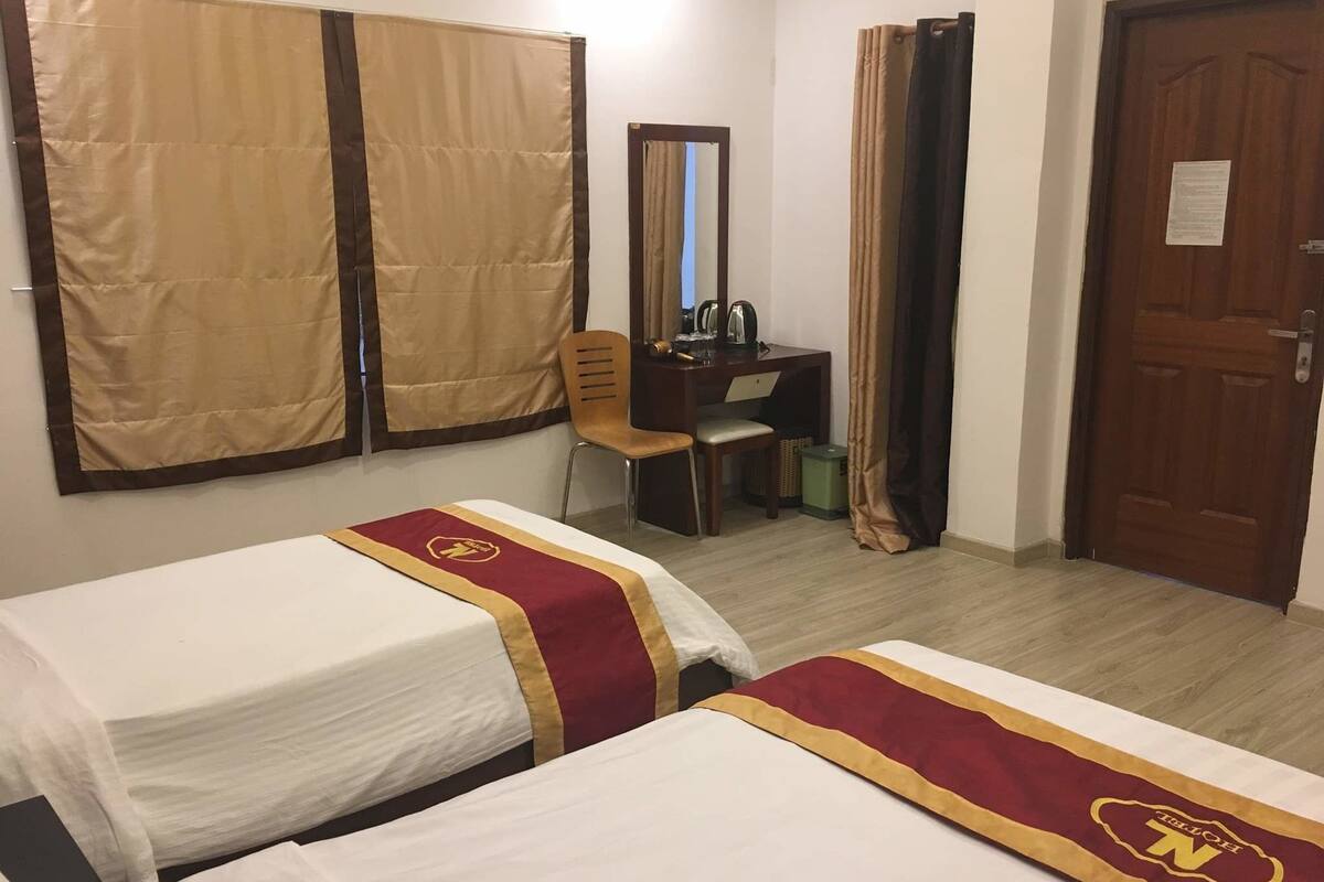 Ein Hotelzimmer mit zwei Betten, einem Schreibtisch, einem Stuhl, einem Spiegel und einer Tür.