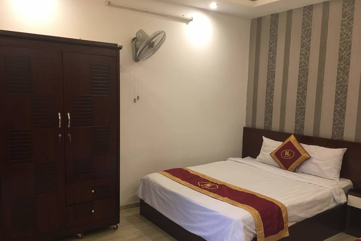 Ein Hotelzimmer mit großem Kleiderschrank, einem Bett mit rotem und goldenem Bettbezug und einem gestreiften Wandmuster.