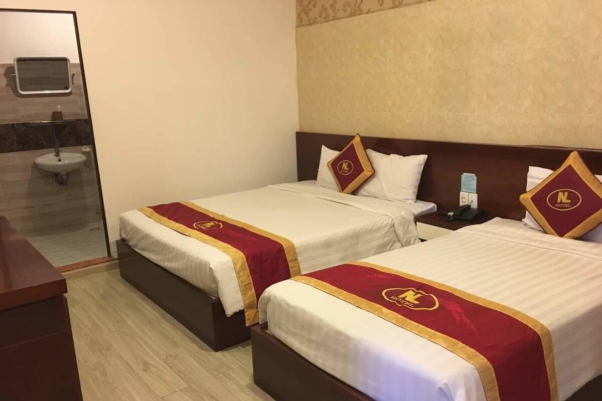 Ein Hotelzimmer mit zwei Betten, jeweils mit roter und goldener Bettdecke, einem Holz-Kopfteil und einem kleinen Nachttisch.