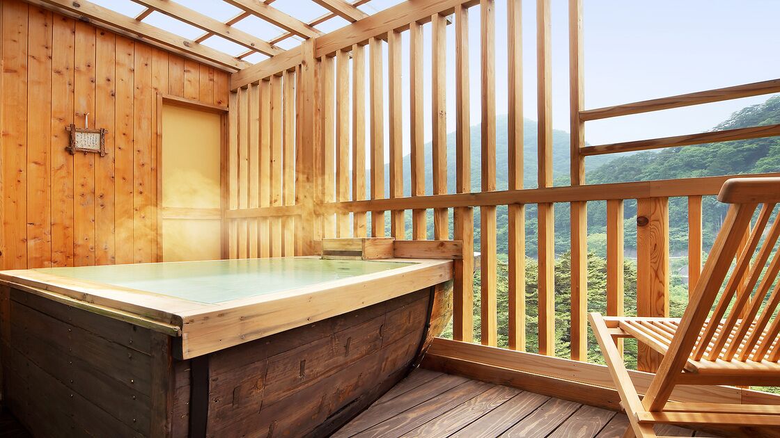Un spa con sala de madera, una bañera de madera, una silla de madera y vista a un paisaje boscoso.