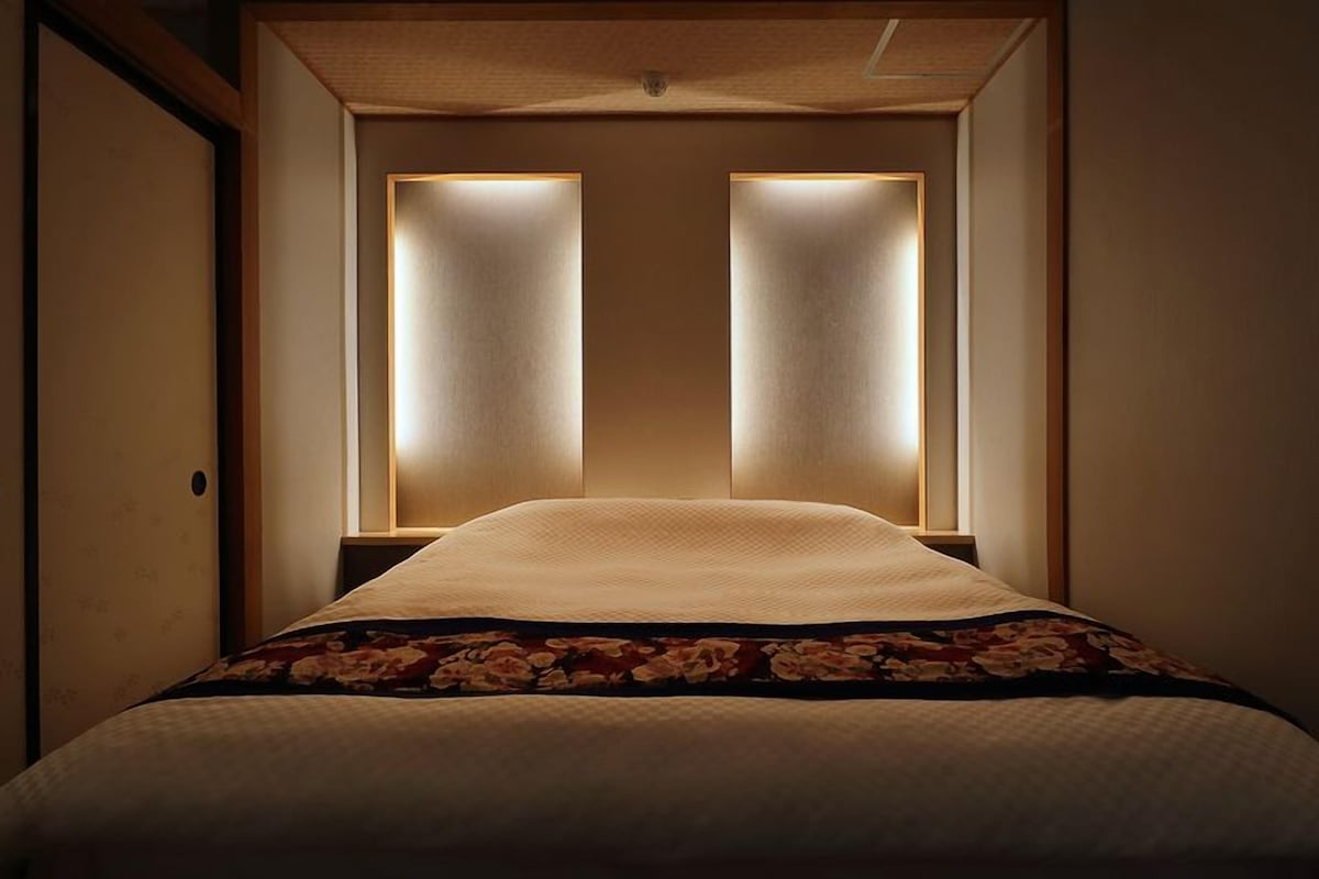 Ein Hotelzimmer mit einem Bett, einer Holztür und zwei beleuchteten Tafeln darüber.