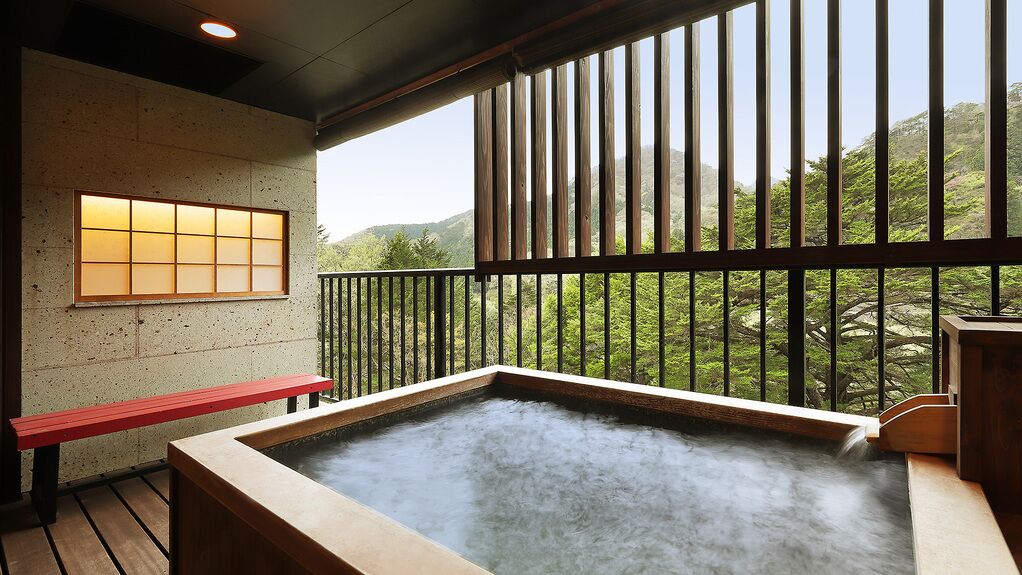 A hot spring area with a wooden bench, a view of greenery, and a traditional Japanese window.