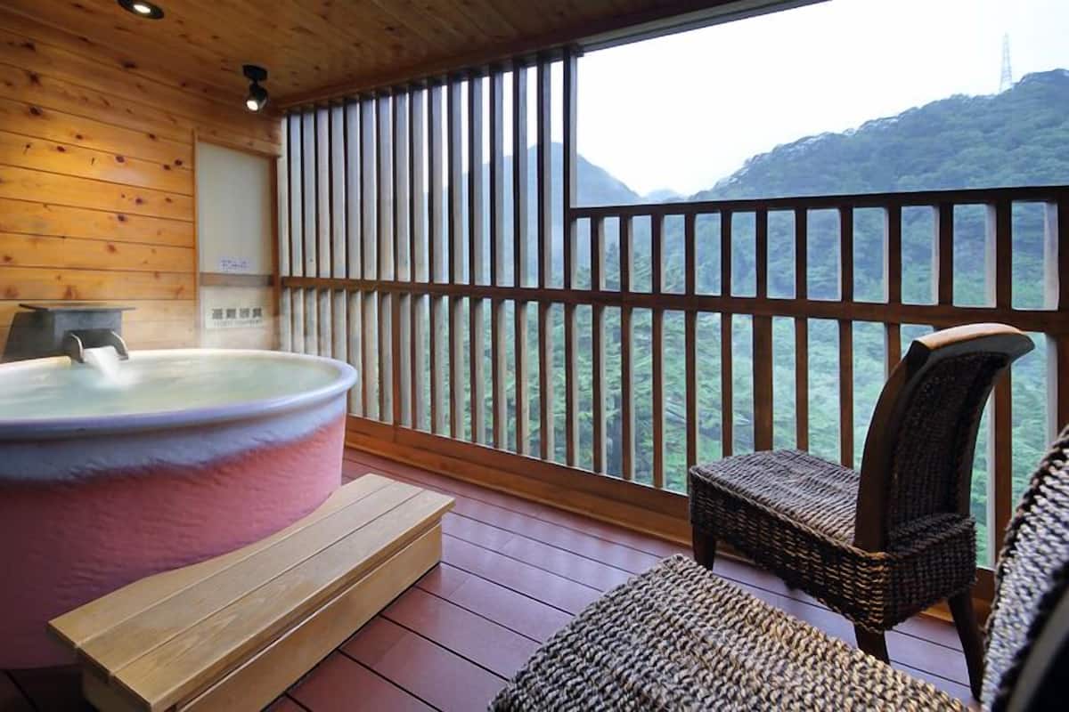 Quarto de madeira com banheira de hidromassagem, uma cadeira e vista para uma montanha.