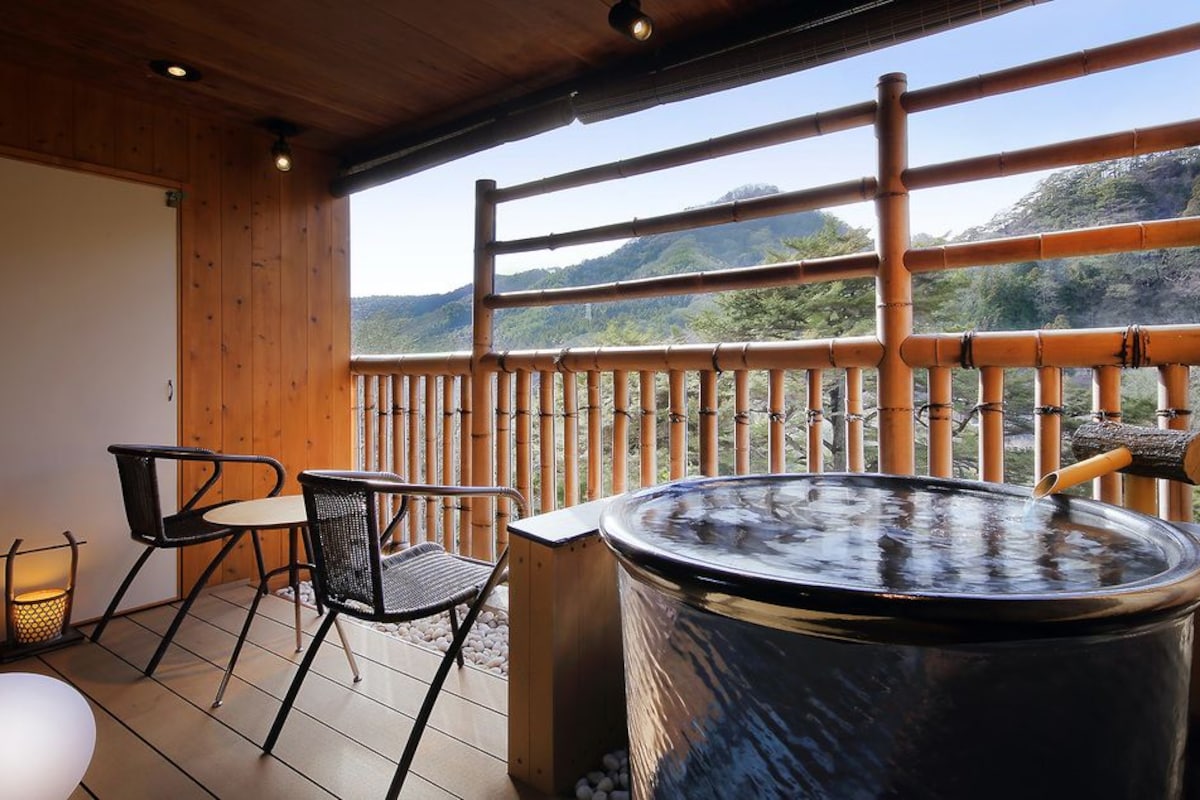 A wooden deck with a hot tub, chairs, and a view of mountains.