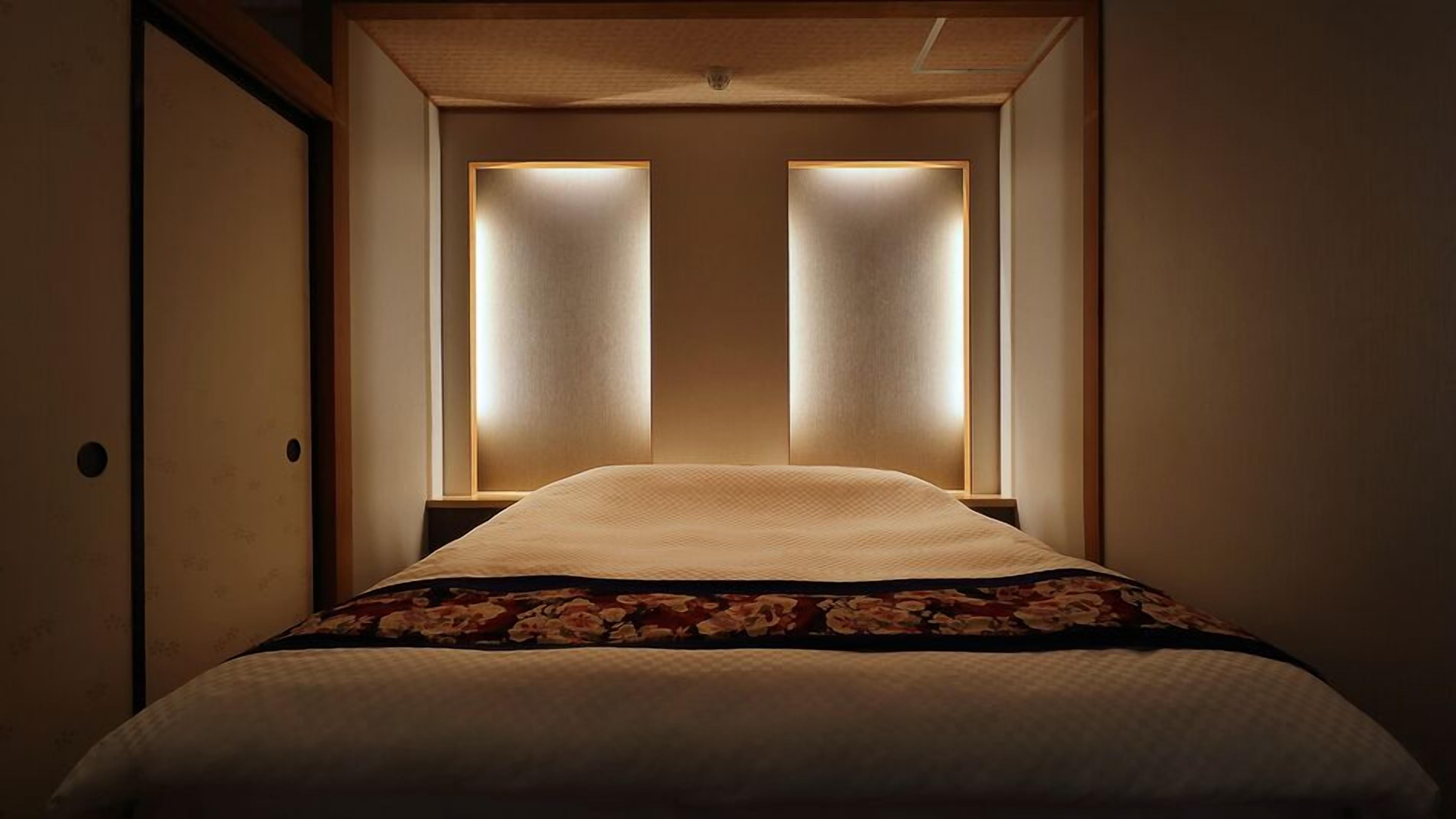 Habitación de hotel con una cama, una puerta de madera y dos paneles iluminados encima de la cama.