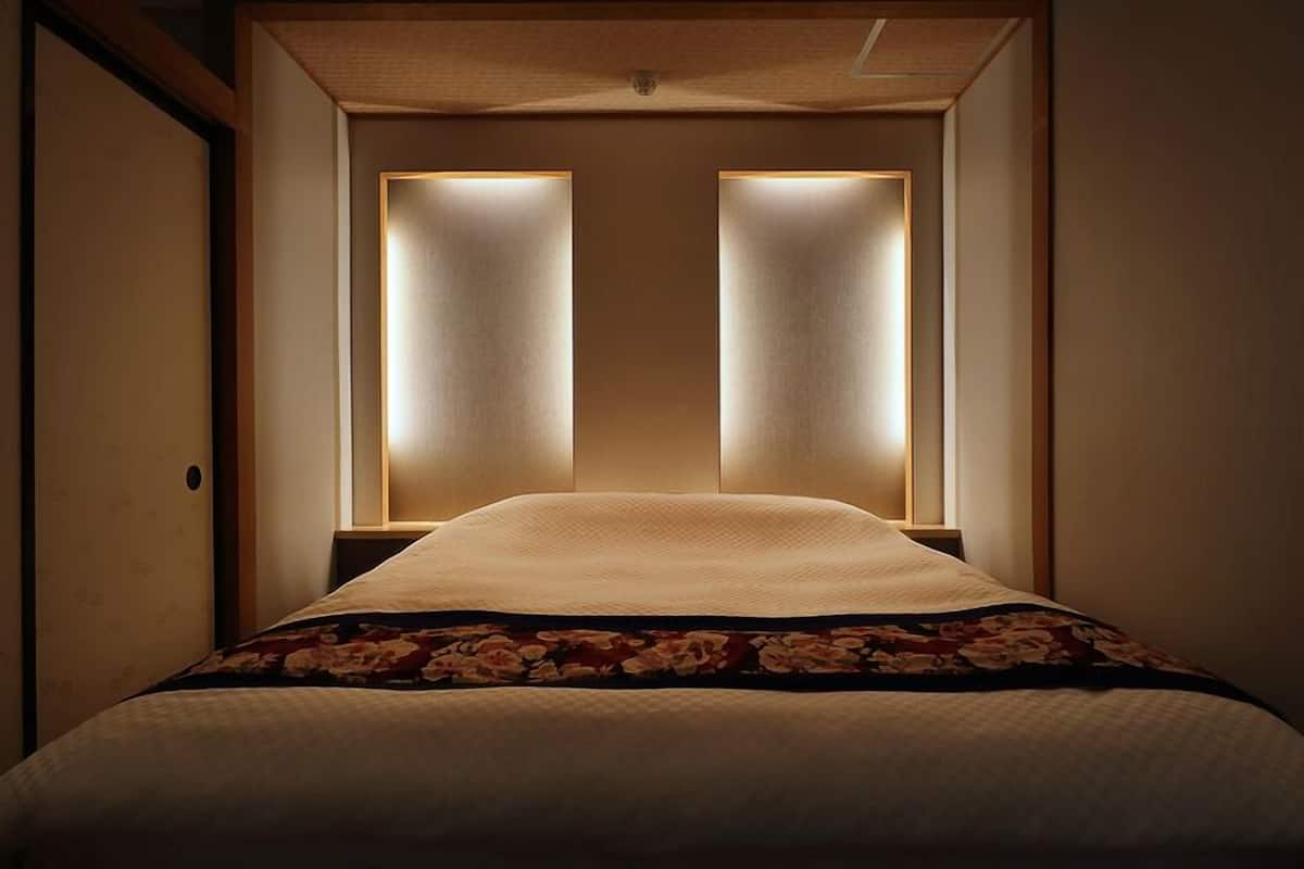Quarto de hotel com uma cama, uma porta de madeira e dois painéis iluminados acima da cama.