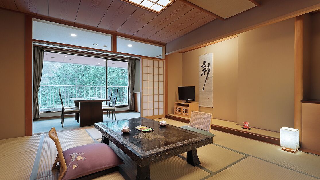 A traditional Japanese room with tatami flooring, a low table, a sofa, a television, and a sliding door leading to a balcony.