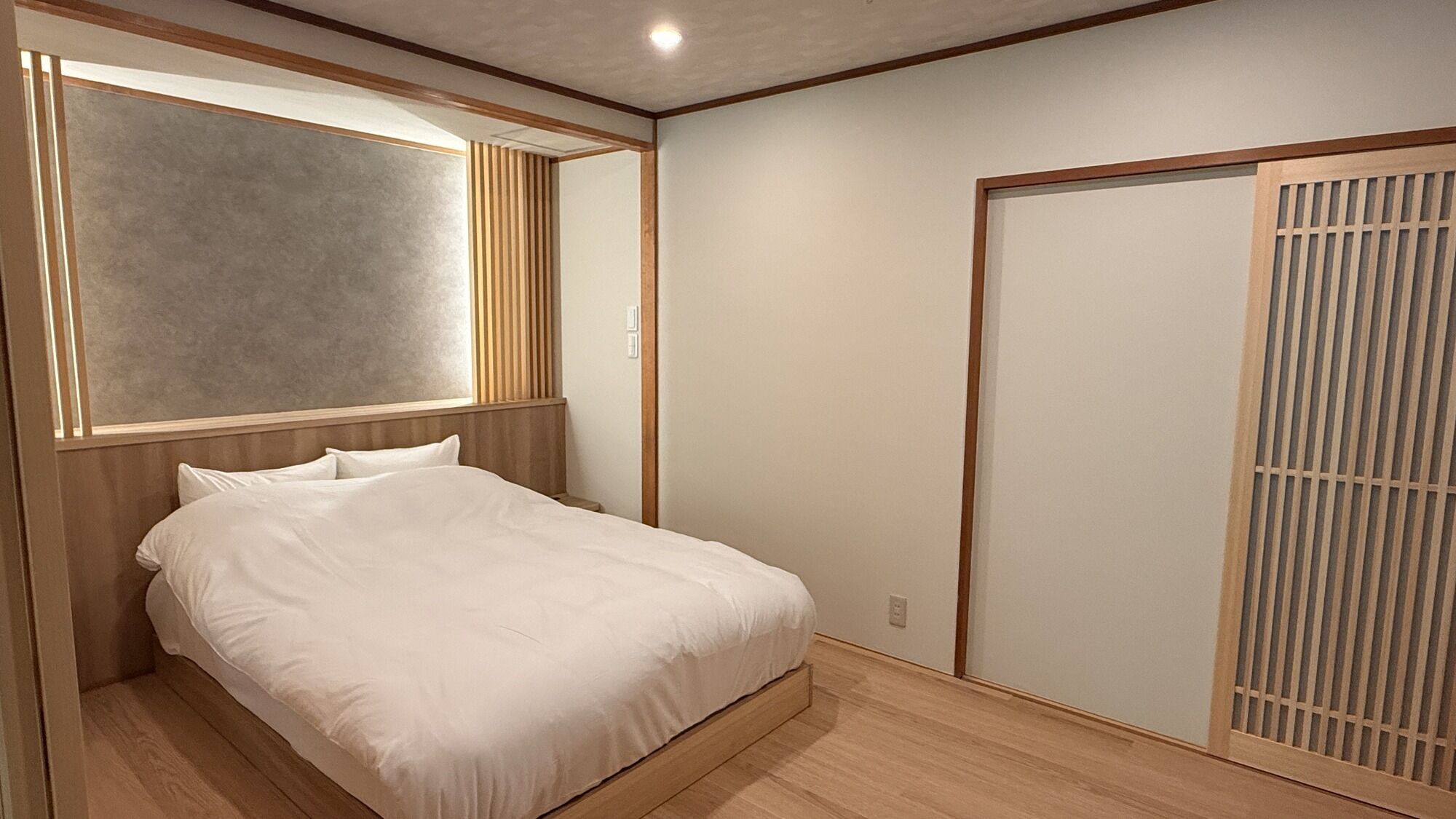 A bedroom with a bed, a wooden headboard, a wall-mounted light, and a sliding door with a vertical pattern.