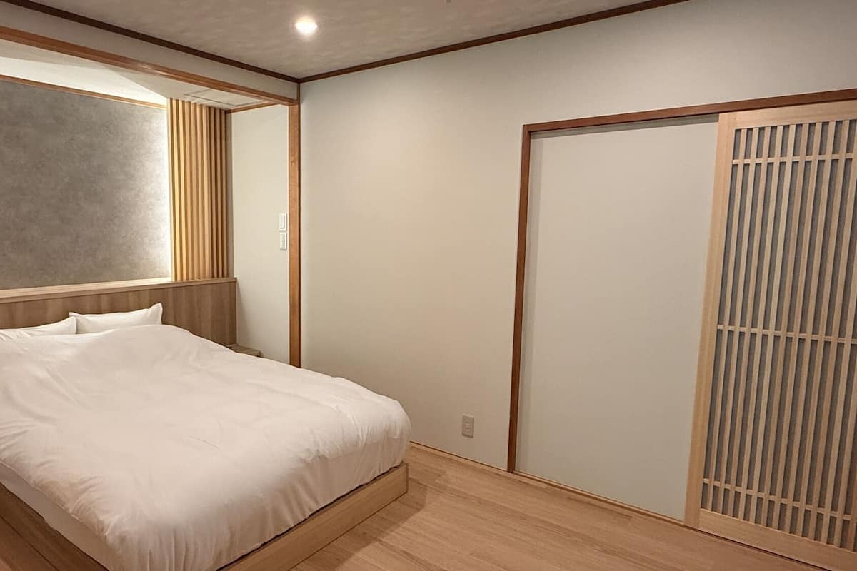 Quarto com cama, cabeceira de madeira, luminária na parede e porta deslizante com padrão vertical.