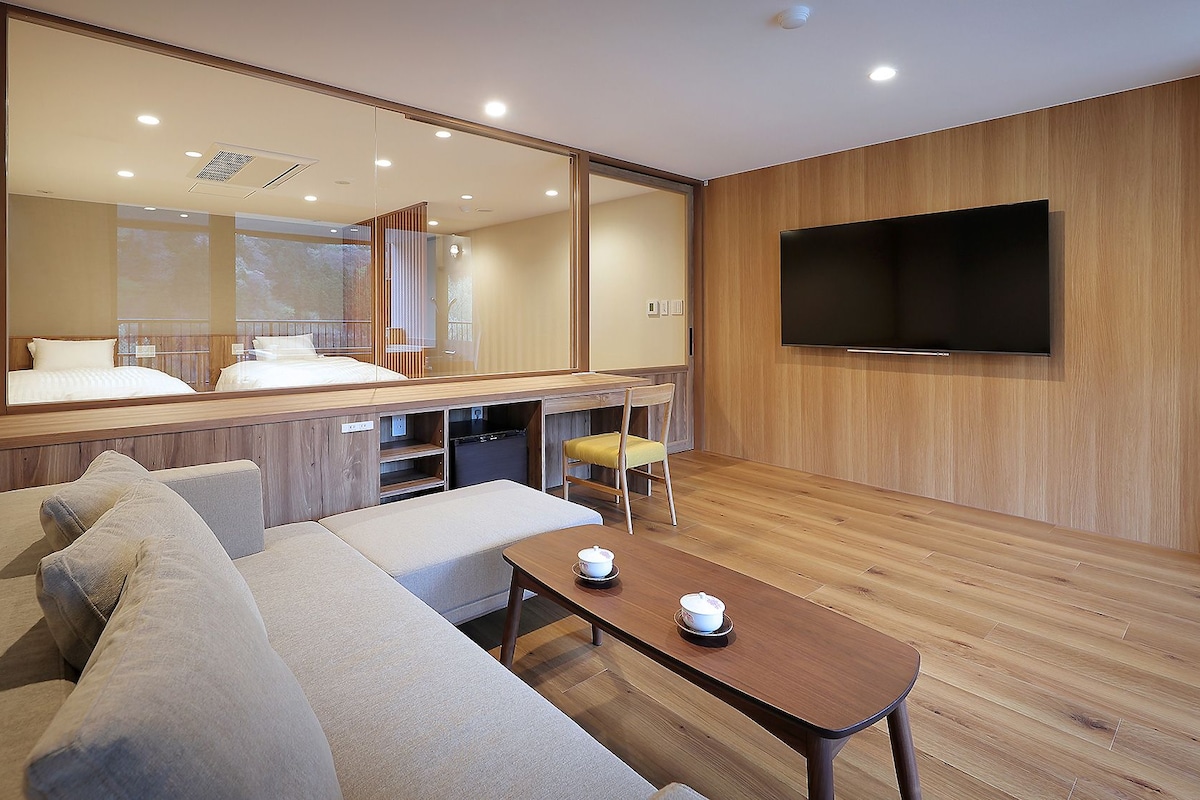 A modern hotel room with a sofa, a small table with cups, a TV, and a large mirror.