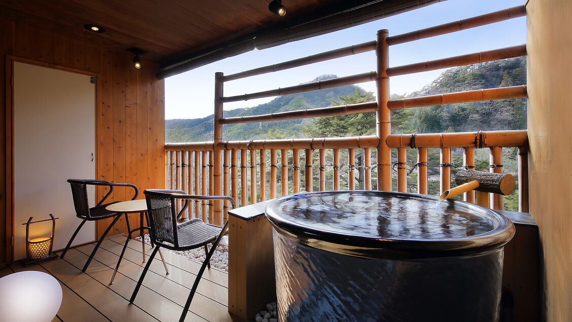 A wooden deck with a hot tub, chairs, and a view of mountains.