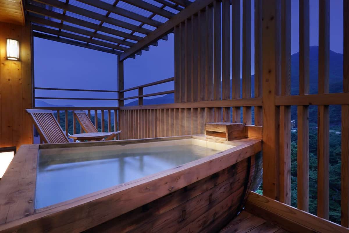 Uma banheira de hidromassagem de madeira com estrutura de vidro, deck de madeira e vista para as montanhas.