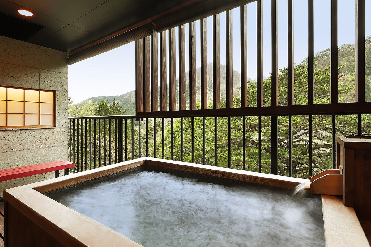 Ein Thermalbereich mit einer hölzernen Bank, Blick ins Grüne und einem traditionellen japanischen Fenster.