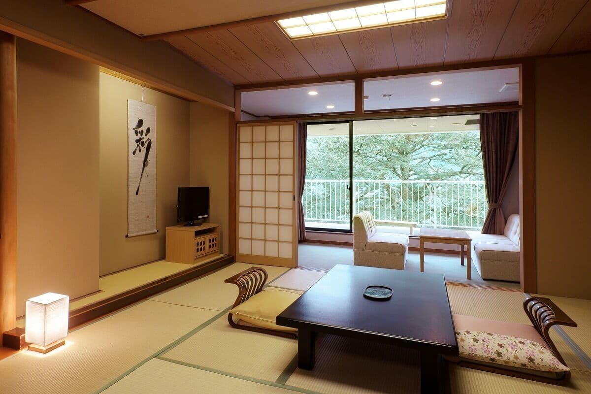Um quarto japonês tradicional com tatames, uma mesa baixa, um sofá e uma porta deslizante que dá para uma varanda.